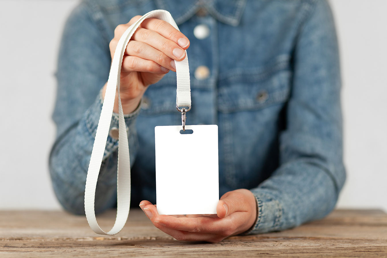 A person in a jean shirt holds a white badge attached to a lanyard.